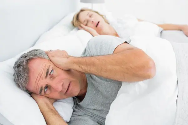 Annoyed man holds his hands over his ears while wife snores next to him