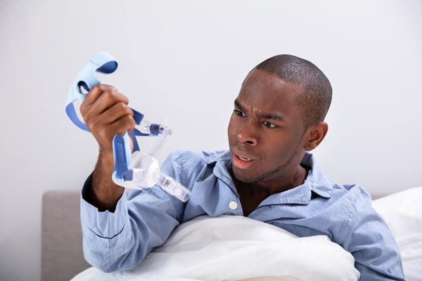 young adult man holding his cpap mask in frustratiob